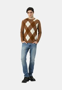 Maglione marrone a motivo argyle con diamanti crema e beige, maniche lunghe, collo rotondo, abbinato a jeans blu e scarpe nere. Maglione semplice, lavorato a maglia testurizzata.