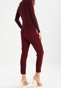 Bordeauxrotes, geripptes Langarmoberteil, kombiniert mit passenden, schmal geschnittenen Hosen und Sandalen mit Metallic-Absätzen. Glatter Stoff mit figurbetonter Silhouette.