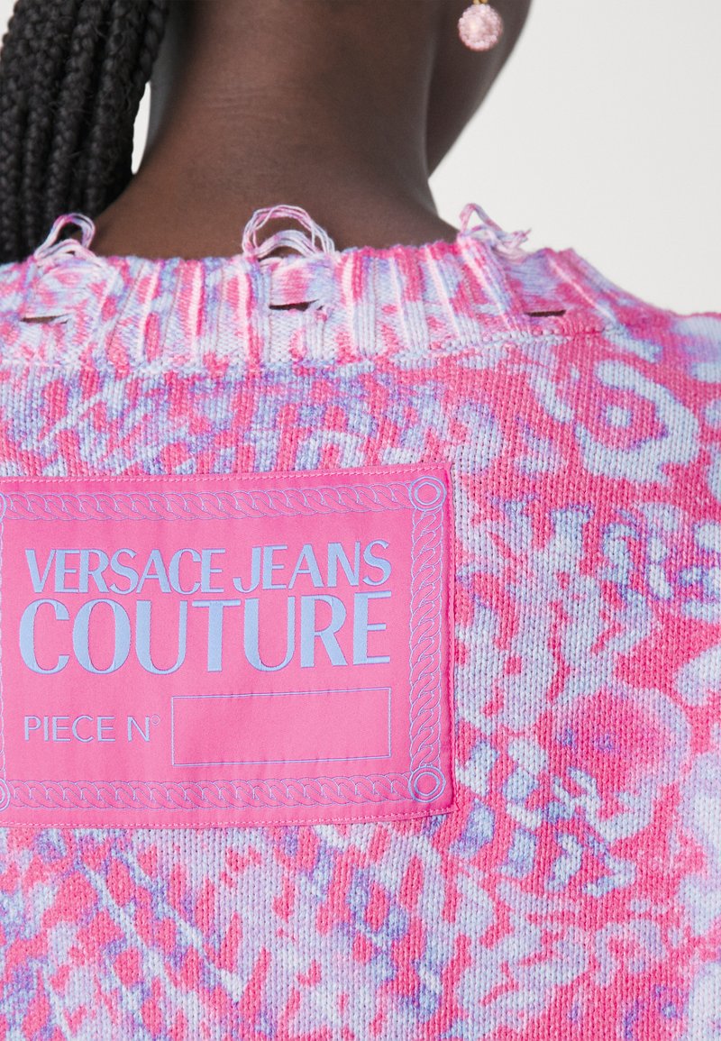 Kleurvolle gebreide trui in roze, met een gevarieerd abstract patroon. Inclusief een roze label met witte tekst "VERSACE JEANS COUTURE." Geweven afwerking.