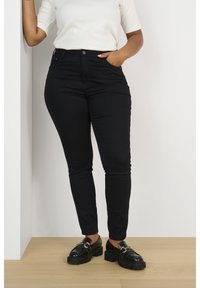 Jean skinny noir en denim, taille haute, doté de cinq poches et d'une fermeture à bouton. Assorti avec des mocassins noirs à semelles épaisses.
