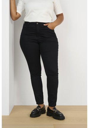 Pantalones vaqueros ajustados negros de cintura alta, con cinco bolsillos y cierre de botón. Combinados con unos mocasines gruesos negros.