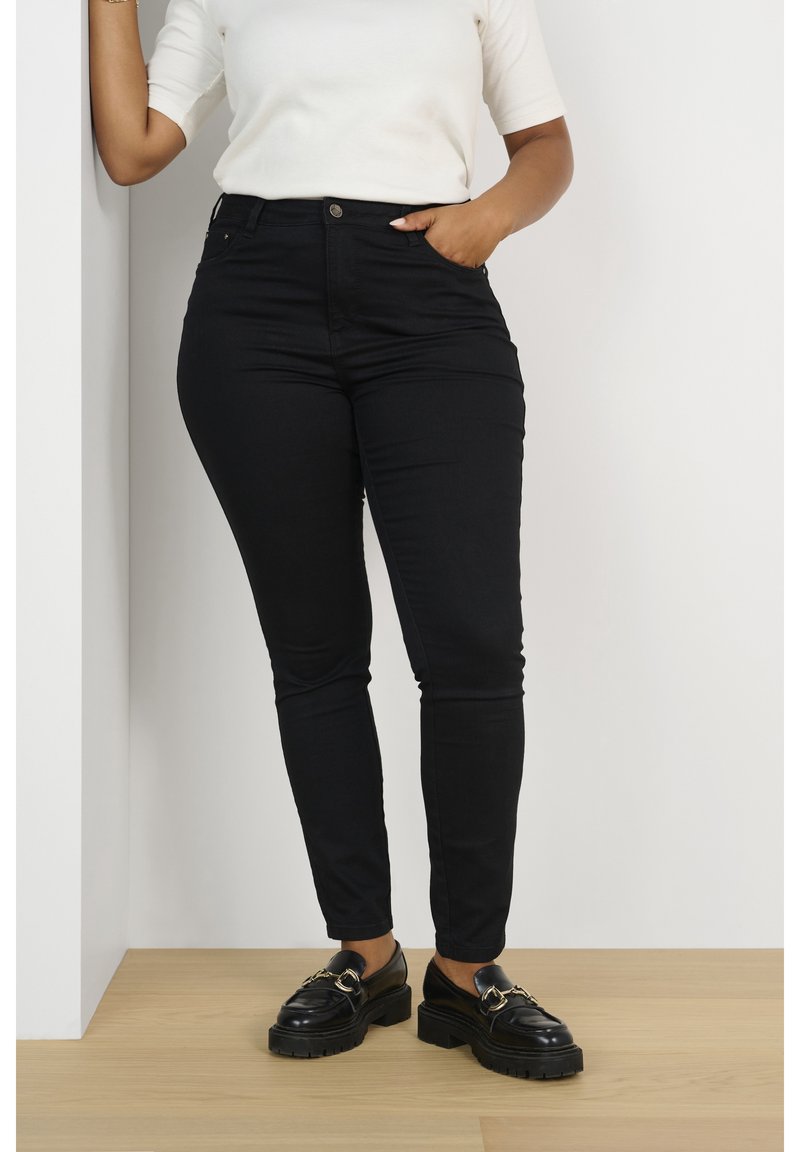 Jean skinny noir en denim, taille haute, doté de cinq poches et d'une fermeture à bouton. Assorti avec des mocassins noirs à semelles épaisses.