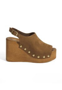 Bruine suede wedge sandaal met een open teen, versierd met gouden metallic studs aan de zijkant en een houten plateauhak. Verstelbare enkelband.