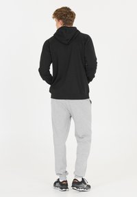 Mustat hupparit, joissa on rento malli, harmaat verkkareita ja mustat urheilukengät, joissa on ribbireunat ja hihansuut, nähtynä takaa.