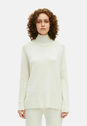 Pull à col roulé surdimensionné en maille crème douce avec des bords côtelés et un ourlet, présentant une texture lisse et un design décontracté.