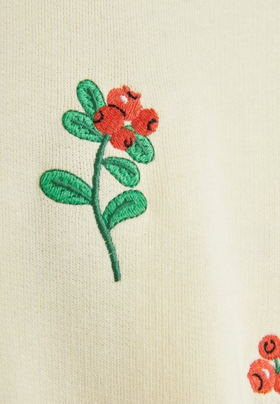 Design floreale ricamato con fiori rossi e foglie verdi su uno sfondo di tessuto beige chiaro. Texture liscia con cuciture visibili.