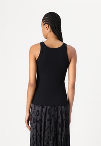 Top negru fără mâneci, cu un design ajustat, bretele late și o textură netedă, combinat cu o fustă pliată cu un imprimeu animalic în nuanțe întunecate.