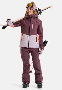 Ski outfit in burgundy and light pink tones, featuring a hooded jacket with zippered pockets and matching pants, paired with ski goggles.