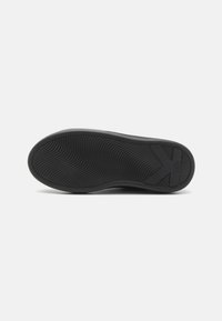 Black rubber shoe sole featuring a wave pattern with textured grip, branded logo, and a rectangular cutout on one side.