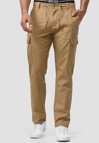 Pantalons cargo kaki à coupe décontractée, dotés de poches latérales, d'une taille avec cordon de serrage et fabriqués en tissu léger. Associés à des baskets blanches.