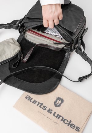 Sac en cuir noir avec des compartiments intérieurs, détails en zip rouge et une doublure douce noire. Comprend une petite pochette rayée et un sac de protection en tissu.