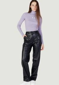 Paarse geribde turtleneck en zwart hooggezoomde faux leer broek met voorzakken. Model draagt witte sneakers.