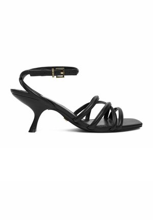 Sandalia de tiras de cuero negro con tacón curvado de altura media y correa ajustable en el tobillo con hebilla dorada, vista lateral sobre fondo blanco.