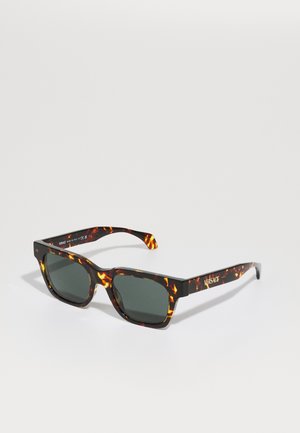 Schildpad zonnebril met donkergroene lenzen, rechthoekige vorm, dikke montuur en gouden "VERSACE" logo op de poot. Glanzende afwerking.