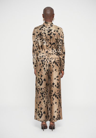 Satin two-piece outfit in gold with black leopard spots, featuring a high neck, long sleeves, and wide-legged trousers.