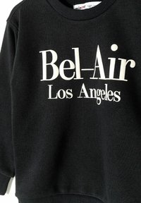 Sudadera negra con puños y cuello acanalados. En la parte frontal presenta grandes letras blancas que dicen "Bel-Air Los Ángeles".