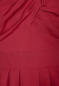 Rotes Kleid mit strukturiertem Stoff, diagonalen Falten, einem gedrehten Design am Oberteil und einer taillierten Silhouette.