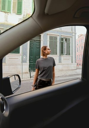 Jonge vrouw in donkere kleding staat nabij een versierd Europees gebouw, gezien door een autoruit op een stadstraat.