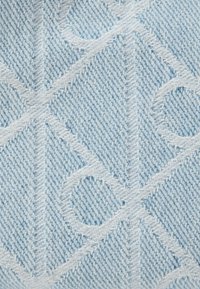 Ανοιχτό μπλε τζιν ύφασμα με γεωμετρικό ανάγλυφο σχέδιο που περιλαμβάνει διαγώνιες γραμμές και κυκλικές διακοσμήσεις. Υφή με εμφανείς λεπτομέρειες ραφών.