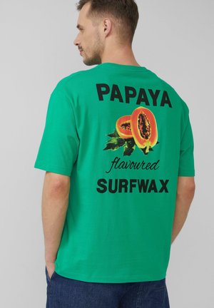 Green short-sleeve t-shirt featuring a large papaya graphic and text reading "PAPAYA flavoured SURFWAX" in black lettering on the back.