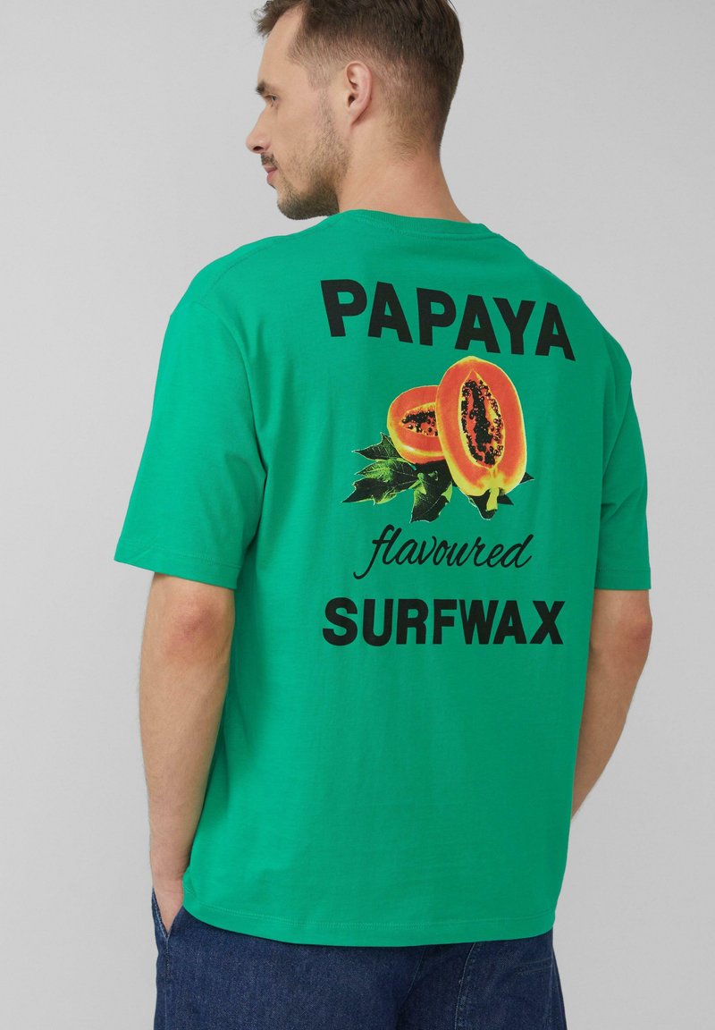 Groene t-shirt met korte mouwen, voorzien van een grote papaya-afbeelding en tekst "PAPAYA-gebruikte SURFWAX" in zwarte letters op de achterkant.