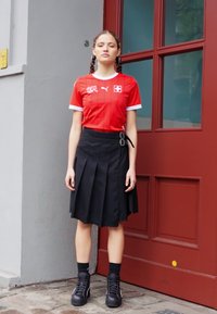 Sarkanais Puma sporta krekls ar baltām akcentiem, apvienots ar melnu drapētu svārku, kuram ir jostas detaļa. Izskatu noslēdz melni kaujas zābaki.