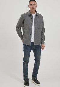 Grå ullblanding jakke med to frontlommer, knappelukking og spiss krage, kombinert med mørkeblå jeans og svarte joggesko.