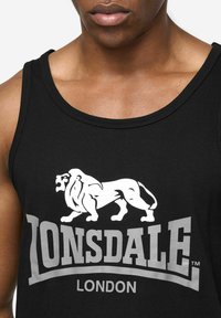 Czarny bawełniany top na ramiączkach z białym logo lwa i srebrnym napisem "LONSDALE LONDON", z okrągłym dekoltem i bez rękawów.