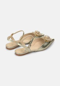 Zapatos planos metálicos dorados con punta afilada, adornados con embellishments de joyas en la parte delantera y una correa en el tobillo para un ajuste seguro.