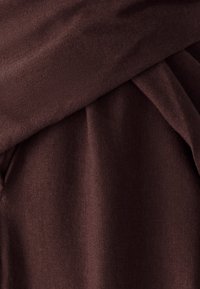 Tissu brun avec une texture douce, présentant des couches drapées et une finition lisse. Le matériau semble léger et flexible.