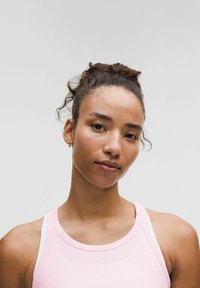 Helles rosa Sporttanktop mit hohem Hals und dünnen weißen Trägern, aus einem strukturierten Stoff. Das Model hat eine natürliche Frisur.