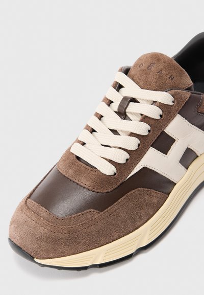 Pruuni ja kreemja värviga sneakerid, millel on suede ja nahast paneelid, valged paelad ning beež tekstuuriga talla lähedalt nurga alt vaadatuna.