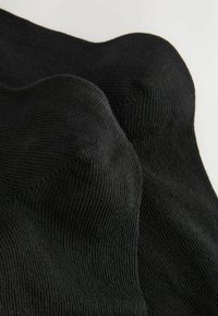 Melnas zeķes ar ribotas struktūras, gludu virsmu un bezšuvju dizainu. Audums izskatās mīksts un elastīgs, lai nodrošinātu komfortu.