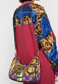 Borsa a spalla multicolore caratterizzata da un motivo trapuntato con accenti dorati. La borsa ha una tracolla a catena e elementi di design a quadri a contrasto.