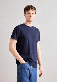 Marineblå t-skjorte med korte ermer laget av mykt stoff, med rund hals og en avslappet passform. Kombinert med lyseblå denimbukser.