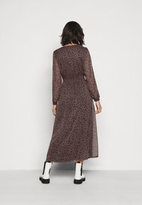 Langärmliges, knöchellanges Kleid mit dunklem Blumenmuster auf durchscheinendem Stoff, tailliert in der Taille und mit einem fließenden Rock. Kombiniert mit weißen Knöchelstiefeln.