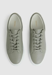 Adidași din piele verde deschis cu șireturi plate, vârf rotund și talpă din cauciuc alb. Include un model texturat subtil și detalii cu logo aurii.
