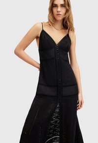 Black dress featuring a fitted bodice with lace detailing, thin straps, a v-neckline, and a button-down front. The skirt is flowy with cutout patterns.
