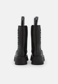 Black ankle boots with a glossy finish, featuring a thick sole, elastic sides, and white logo accents. Smooth texture and pull tabs.