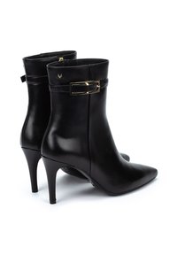 Botas de cuero negro hasta el tobillo con puntera afilada, tacón de aguja y un acento de hebilla dorada en el tobillo. Textura suave, diseño elegante.