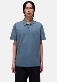 Polo azul claro en material de algodón, con placket de tres botones, mangas cortas y pequeño logo bordado en el pecho.