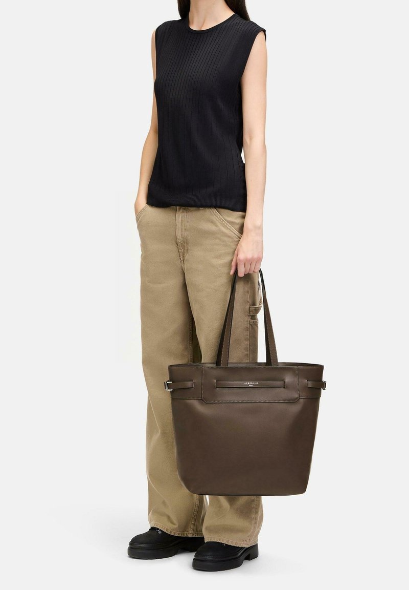 Brun läder tote-väska med en strukturerad form, dubbla handtag och detaljerad frontpanel. Kombinerad med en svart ribbad ärmlös topp och khakifärgade byxor.