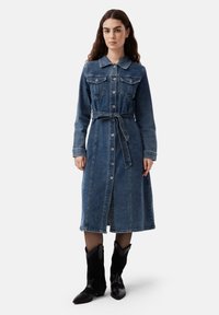 Rochie lungă din denim de culoare albastru închis, cu nasturi în față, buzunare în zona pieptului și talie cu curea. Are un guler și mâneci lungi.