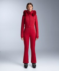 Rood eendelig skipak met bont gevoerde capuchon, nauwsluitende silhouet, ritssluiting en uitlopende pijpen, gecombineerd met zwarte skischoenen.