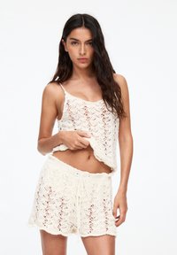 Crocheted two-piece set in creamy white, featuring a sleeveless top with a scalloped hem and matching shorts with a drawstring waist.