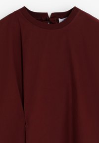 Bordeaux top met een ronde halslijn en een knoopsluiting op de achterkant. Voorzien van lange mouwen en een gladde, gestructureerde stof.