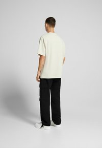 Beige oversize t-shirt med korta ärmar, kombinerad med svarta cargo-byxor med fickor och vita sneakers. Enkel, avslappnad outfit.