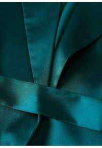 Gros plan d'un tissu satin bleu sarcelle avec des plis qui se chevauchent et une large ceinture au centre.