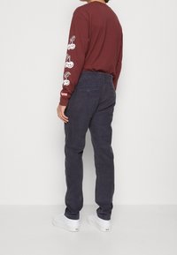 Mörkröd långärmad skjorta med vita körsbärsgrafiker på ärmarna, i kombination med mörkblå byxor och vita sneakers. Minimalistisk design, avslappnad passform.