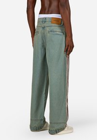 Svijetloplavi traperice širokih nogavica, s bijelim pojasom, kontrastnim bočnim trakama i kožnom etiketom na stražnjoj strani.